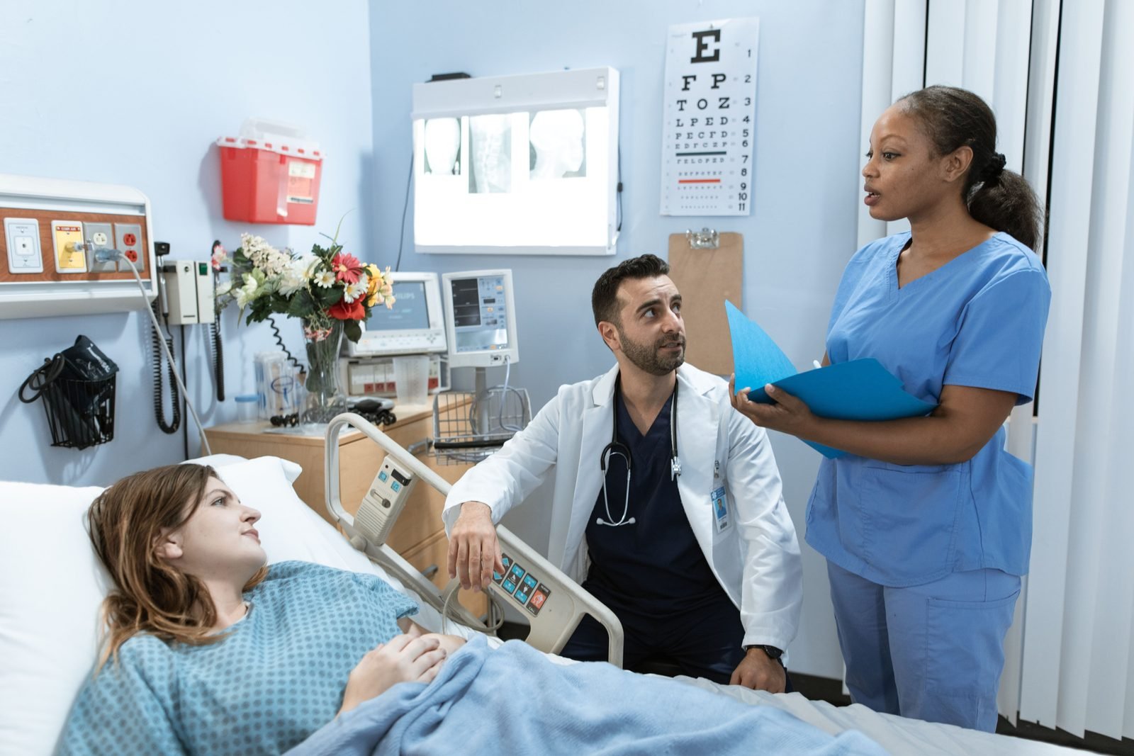 A doctor and a nurse talking with a patient in a hospital room