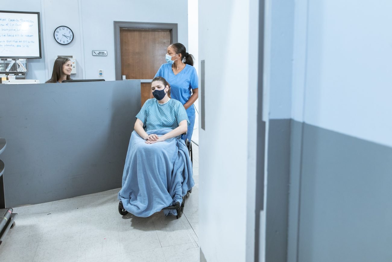 A nurse bringing a patient in a wheelchair to the reception desk